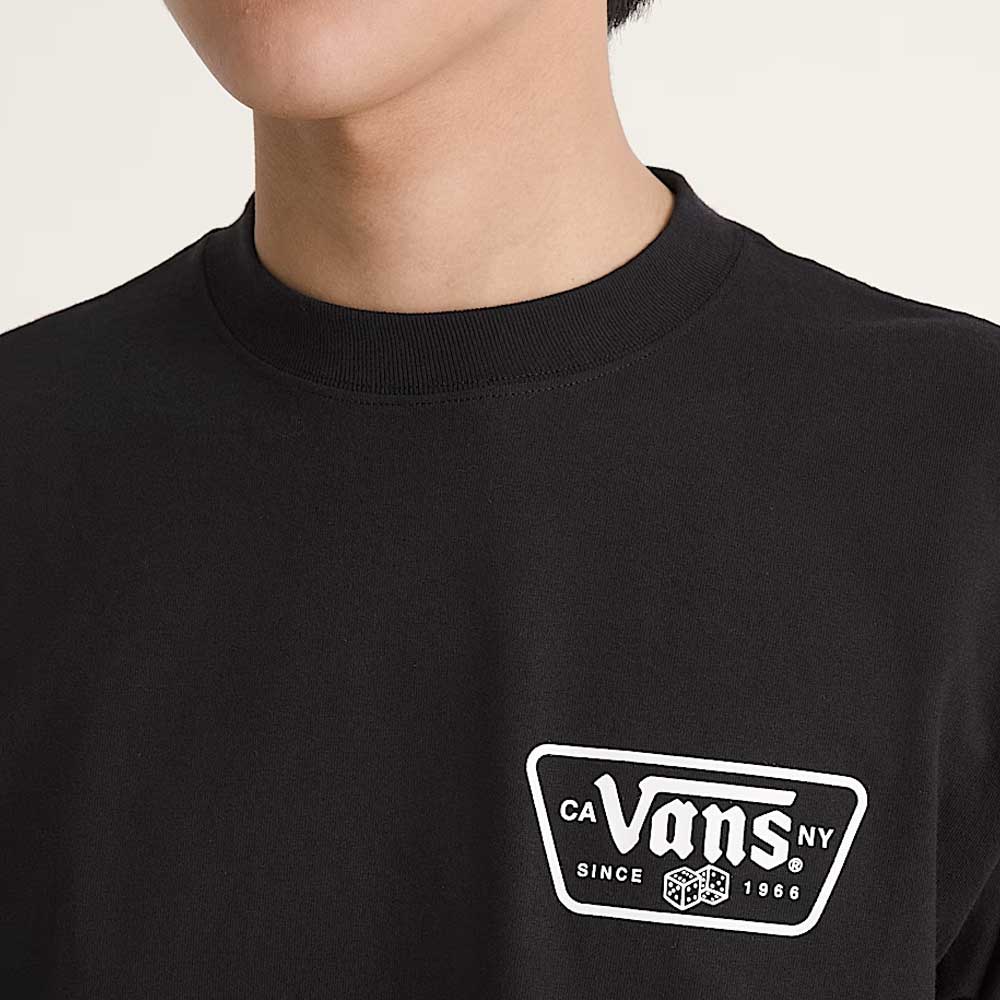 A person is wearing a Knu Patch VN000WU8BLK1 Black Short Sleeve Tee from Vans Skateboarding, featuring a white logo on the chest; only their lower face and upper torso are visible.