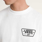 A person wears the Knu Patch VN000WU8WHT1 White Short Sleeve Tee by Vans Skateboarding, featuring a loose fit, 100% cotton, with a black Vans logo, CA NY SINCE 1966 text, and dice graphic on the chest; face partially out of frame.