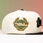 The La Cumbia WS05 Chrome Black Mexico Houston Astros New Era 59FIFTY Fitted Hat features a cream crown with a black brim and is adorned with a gold and green World Series logo patch depicting a globe and laurel wreath—an ideal accessory for Houston Astros fans.