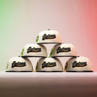 Six La Cumbia WS05 Chrome Black Mexico Houston Astros New Era 5950 Fitted hats, featuring a cream colorway and bold Astros branding—ideal for Houston Astros fans—are stacked in a pyramid arrangement against a backdrop illuminated by gradient red and green lights, creating a dramatic, Chrome Black-inspired display.