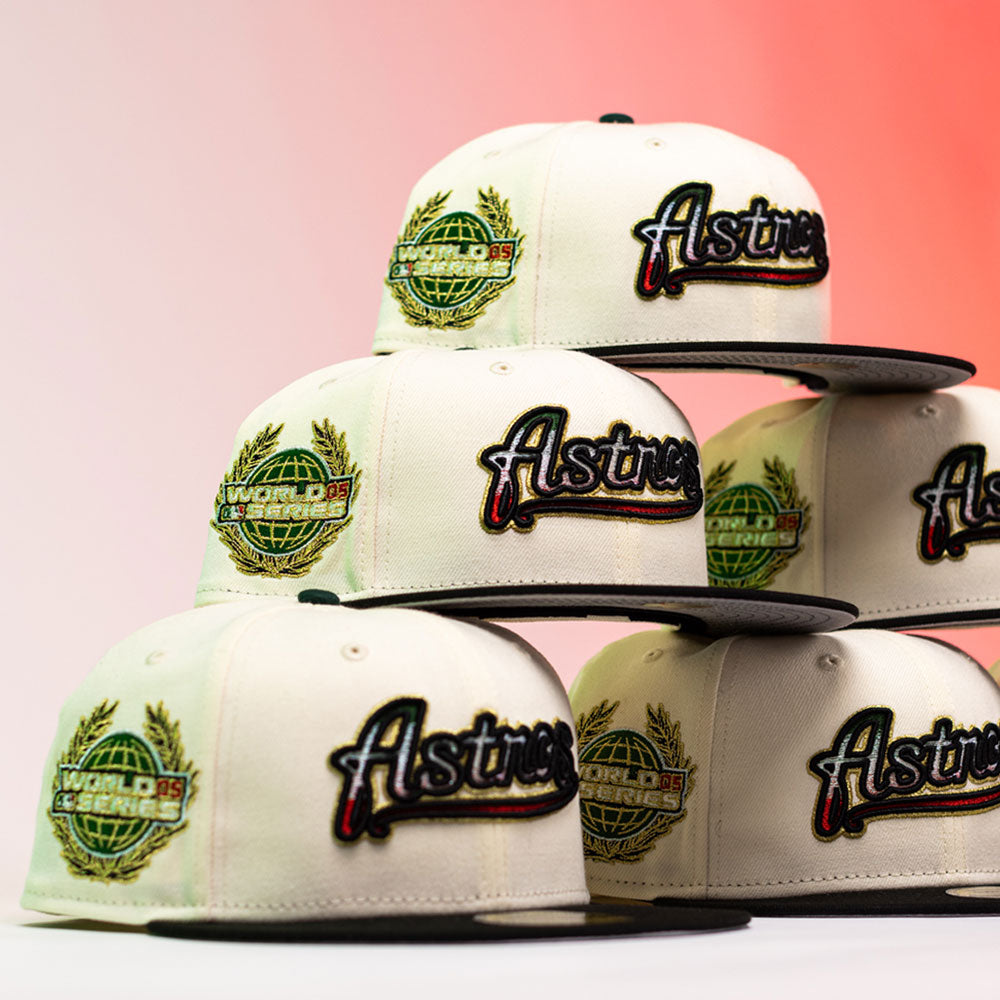 Five La Cumbia WS05 Chrome Black Mexico Houston Astros New Era Hat 5950 Fitted caps are stacked together, each showcasing the iconic Astros logo and a World Series Champions patch on the front. The cream-colored hats feature sleek black brims and Chrome Black details, accentuated by a softly fading white to pink background that enhances their modern style.