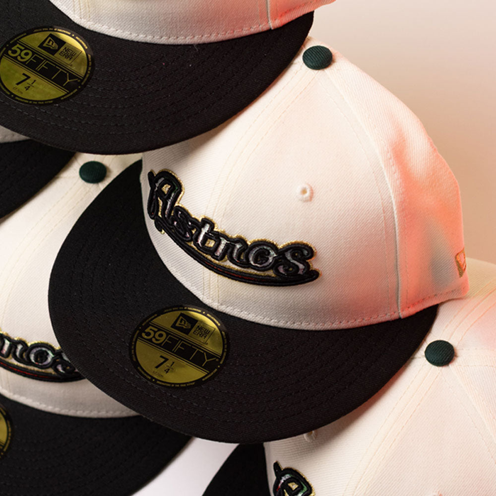 A stack of La Cumbia WS05 Chrome Black Mexico Houston Astros New Era 5950 Fitted hats, in black and white, showcases the Houston Astros embroidery on the front. Each Chrome Black cap displays a gold 59FIFTY sticker on its black brim.