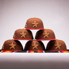 Six Bendicion de la Abuela 20th Brown Red Houston Astros New Era Hat 5950 Fitted caps, featuring yellow star logos, are stacked in a pyramid on a plain background with a colorful cloth at the base.