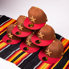 Six Bendicion de la Abuela 20th Brown Red Houston Astros New Era Hat 5950 Fitted caps with yellow star logos are stacked pyramid-style on a colorful striped fabric.