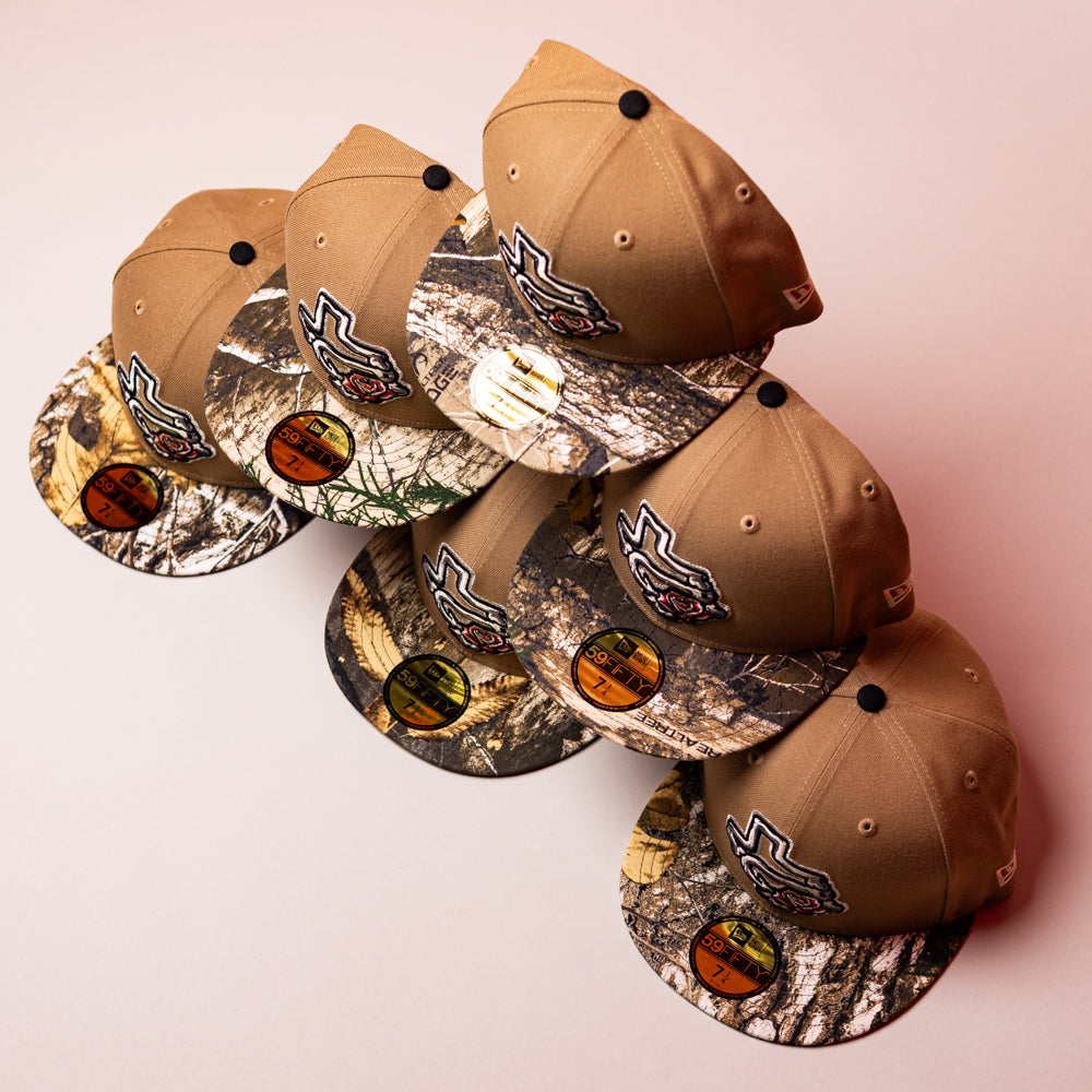 Five La Ofrenda Khaki RTC Copa Corpus Christi Hooks New Era 5950 Fitted hats, featuring camouflage brims and embroidered logos, are arranged diagonally on a pink surface, each with a sizing and branding sticker on the brim.