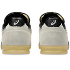 Back view of Leggerezza Asics Oyster Grey Black 1203B087 020 Suede Skateboarding Shoes with a light beige suede upper, black heel tabs with white ASICS logo, and translucent gum soles—echoing classic Asics soccer cleat design.