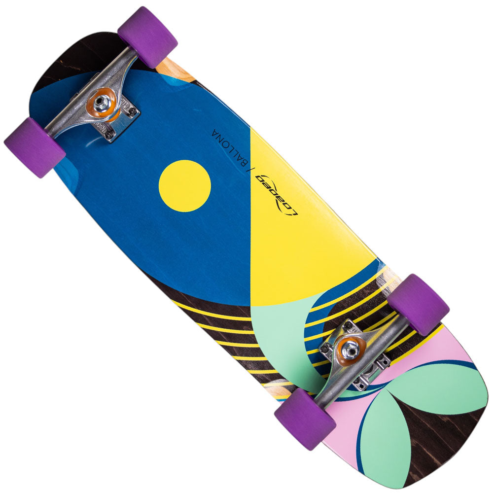 The Loaded Ballona 9x27.5 Complete Longboard features a compact deck with abstract blue, yellow, green, pink, and black patterns, a yellow dot, purple wheels, and the word BALIONA printed on it.