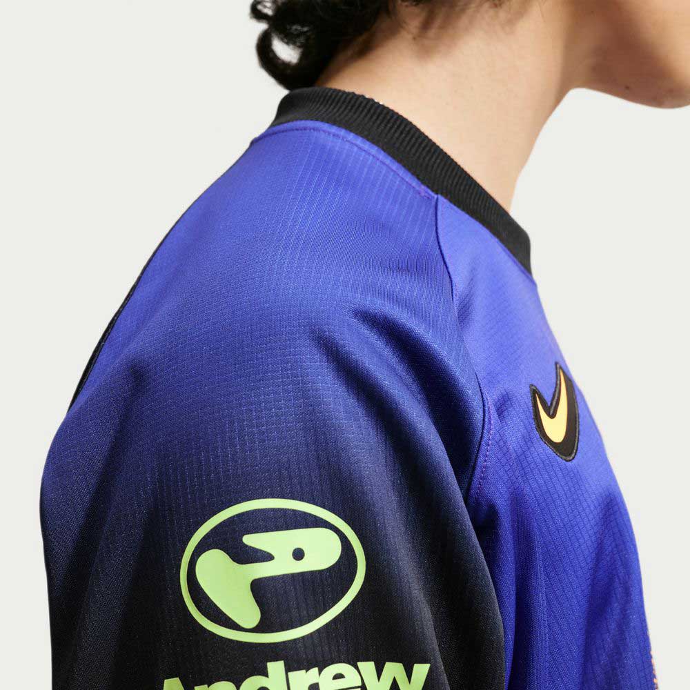 A person wears the Nike SB Long Sleeve Skate Top IQ6594514, a blue jersey with a black polyester rib collar, yellow Nike logo on the chest, and "Andrew" on the sleeve. It's imported, machine washable; photo is side view showing shoulder and head.