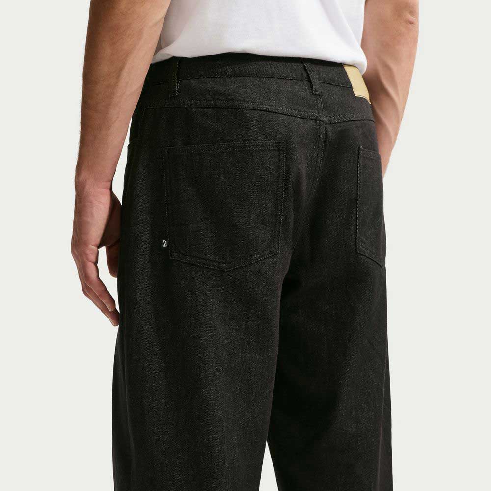 A person is shown from behind, waist down, wearing Nike SB Loose Denim Black Pant IB2992010. The 100% cotton jeans feature two back pockets, a jacron waistband label, and classic styling.