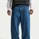 Wearing Loose Denim French Blue Pant II7363487 Nike SB, a person stands against a plain background with hands relaxed by their sides, paired with a black and white striped T-shirt and a white long-sleeve shirt.