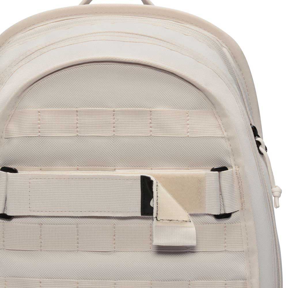 Close-up of the upper front section of the Lt Orewood Brown Black FD7544104 Nike SB RPM Skate Backpack, featuring multiple horizontal webbing straps, a small fabric loop with a black metal clip, and a partially visible zipper on the right.