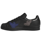 The Mark Gonzales Black Black Black LA6416 Superstar ADV x Gonz Adidas Skateboarding Leather Shoes feature black uppers with matching black laces and are accented by blue and gray bird-shaped patches on the side. Displayed in a left side profile view against a white background, these shoes offer a distinctive take on classic skateboarding style.