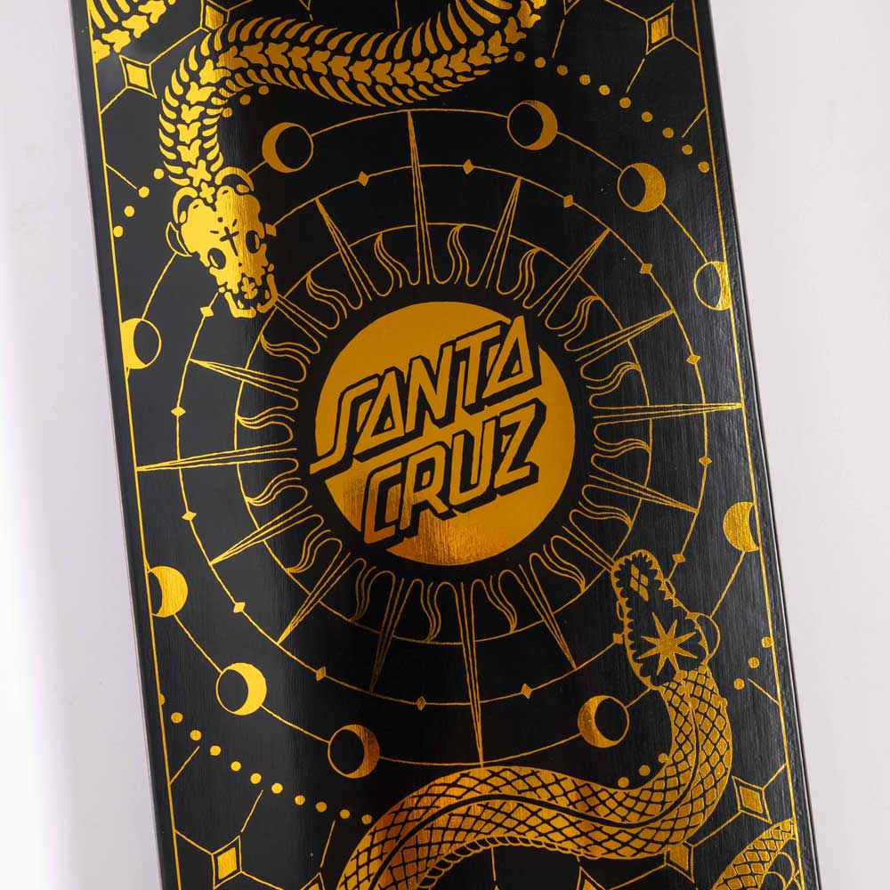 Close-up of the McCoy Snakes VX Deck 8.25in x 31.83in by Santa Cruz Skateboards, showcasing a gold geometric snake and celestial design with moons and "Santa Cruz" centered on a black background.