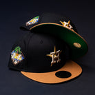 Two Midsummer Night 26 Spring Bronze Houston Astros New Era Hat 5950 Fitted caps, featuring embroidered logos and a commemorative side patch, are stacked on a dark surface against a dark background.