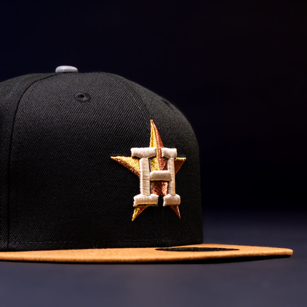The Midsummer Night 26 Spring Bronze Houston Astros New Era 5950 Fitted hat features a black crown, yellow brim, gold and orange star, and bold white “H” on the front, displayed against a dark background.
