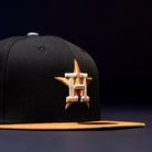 The Midsummer Night 26 Spring Bronze Houston Astros New Era 5950 Fitted hat features a black crown, yellow brim, gold and orange star, and bold white “H” on the front, displayed against a dark background.