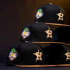 A stack of Midsummer Night 26 Spring Bronze Houston Astros New Era 5950 Fitted hats with black crowns, brown brims, a palm tree patch, and a gold H star logo is displayed against a dark background.