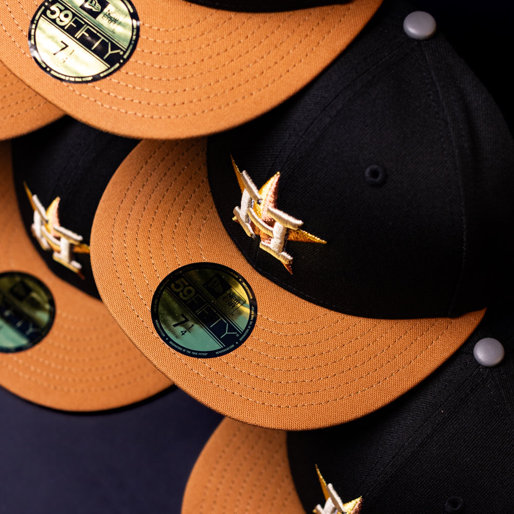 Several Midsummer Night 26 Spring Bronze Houston Astros New Era 5950 Fitted hats are stacked, each featuring a gold H logo and shiny 59FIFTY sticker on the brim.