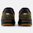 A pair of Mike Gigliotti True Brown Candy Pink 933 LOT New Balance Numeric suede skateboarding shoes viewed from the back, with olive green suede, black midsoles, tan outsoles, and brown and black accents on a light gray background.