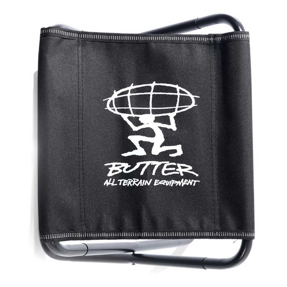 The Mini Packable Camping Chair Black Butter Goods features an aluminum alloy frame, "BUTTER ALL TERRAIN EQUIPMENT" in white, and a figure with a globe design. Folds easily and comes with a carry pouch for portability.