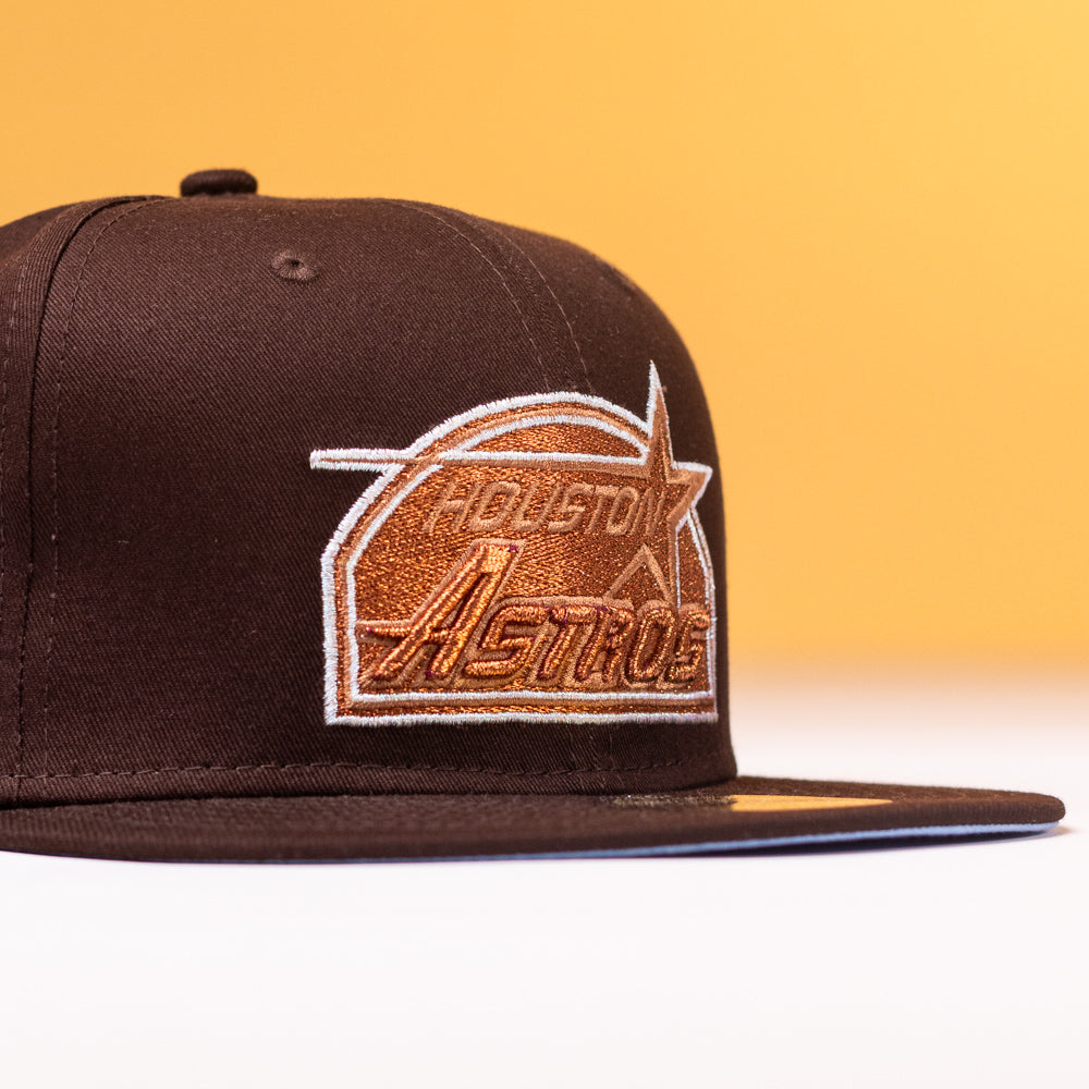 The Muddy Waters Houston Astros New Era Hat 5950 Fitted, featuring an orange and white embroidered logo, is displayed against a yellow background.