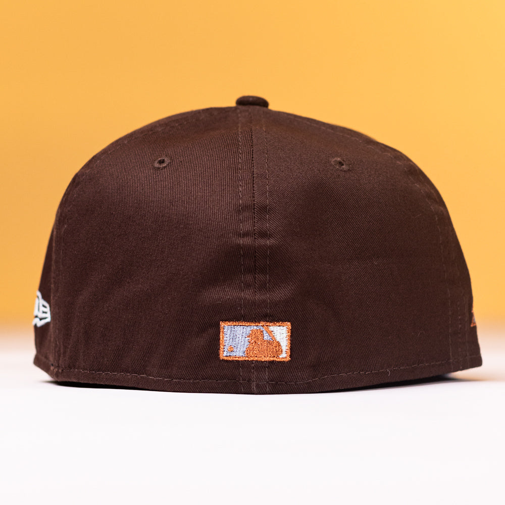 The Muddy Waters Houston Astros New Era 5950 Fitted Hat is displayed with the back facing forward, showcasing a small embroidered patch with a mountain and sky design, set against a yellow background.
