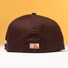 The Muddy Waters Houston Astros New Era 5950 Fitted Hat is displayed with the back facing forward, showcasing a small embroidered patch with a mountain and sky design, set against a yellow background.
