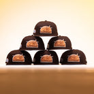 Six Muddy Waters Houston Astros New Era 5950 Fitted hats are stacked in a pyramid shape on a smooth surface, set against a warm yellow gradient background.