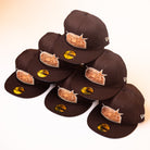 Six Muddy Waters Houston Astros New Era 5950 Fitted hats, featuring black fabric with brown embroidered Houston Astros logos and gold stickers, are stacked in a pyramid shape on a white background.