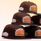Six black Muddy Waters Houston Astros New Era Hat 5950 Fitted baseball caps with copper logos and silver patches are stacked in two uneven columns against a plain, soft beige background.