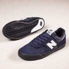 A pair of Jamie Foy Eclipse White 306 NSN New Balance Numeric suede skateboarding shoes, featuring black soles and laces. One shoe stands upright while the other lies on its side, displaying the zigzag tread pattern.
