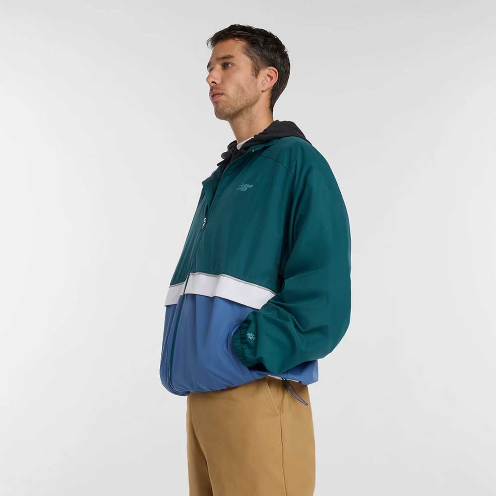 A man stands in profile wearing the New Balance Numeric Jacket MJ61W4XCAAV, made from durable ripstop fabric with NB DRY technology, over a black shirt and tan pants, set against a plain white background.