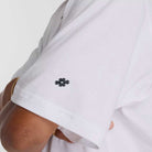 A close-up of a person’s crossed arms in the New Balance Numeric Small Logo White Tee MT53706WT, a relaxed fit cotton crewneck featuring a small black pixel-style hashtag symbol on the sleeve.