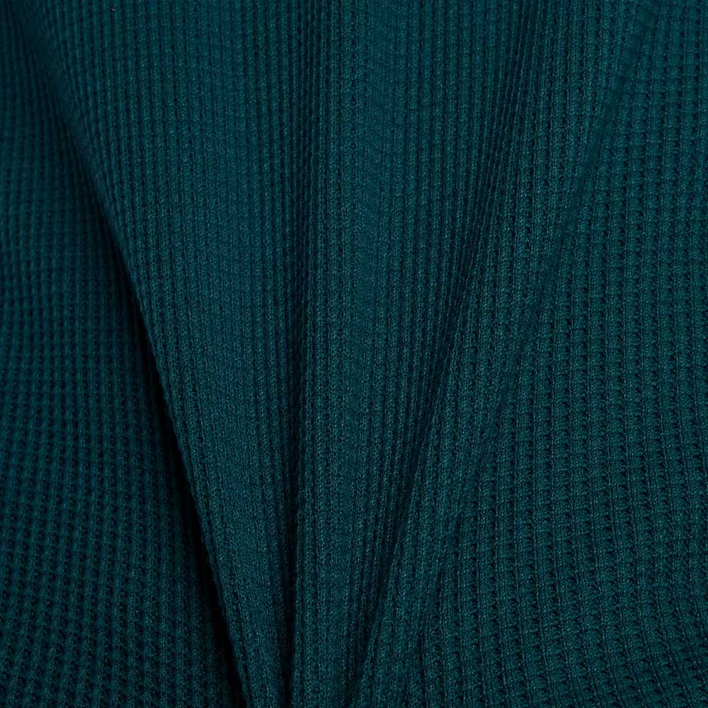 Close-up of the New Balance Numeric Waffle Knit Tee MT51958AAV in dark teal, showing ribbed waffle knit fabric with a central fold that creates a symmetrical, pleated look and highlights its cozy cotton blend texture.