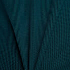 Close-up of the New Balance Numeric Waffle Knit Tee MT51958AAV in dark teal, showing ribbed waffle knit fabric with a central fold that creates a symmetrical, pleated look and highlights its cozy cotton blend texture.