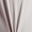 Close-up of the New Balance Numeric Waffle Knit Tee MT51958GYM, featuring light-colored, textured waffle knit fabric with a honeycomb pattern and gentle vertical folds.