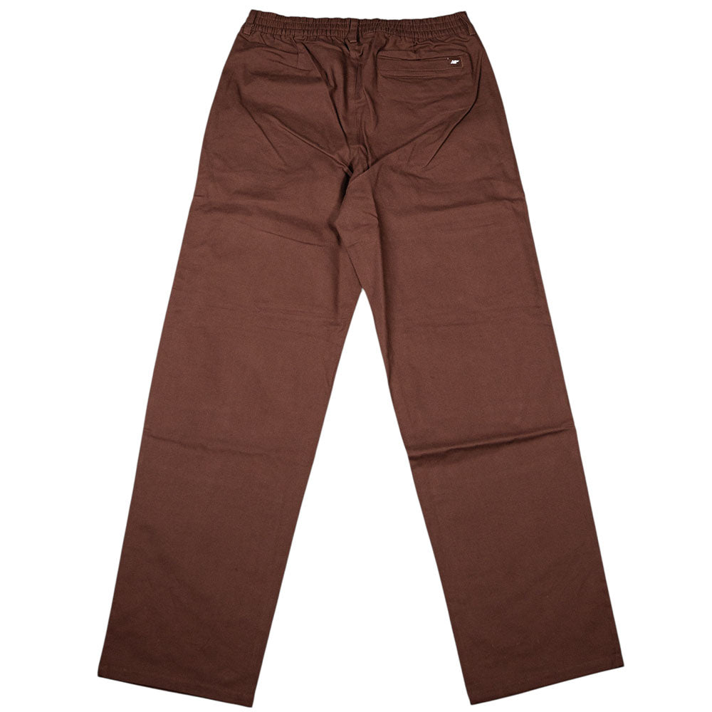 The New Balance Numeric Pant Pumperknickel MP51953ABJ is a brown straight-leg skateboarding pant featuring an elastic waistband, small back pocket, and durable cotton canvas, shown laid flat on a white background.