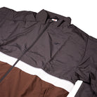 The New Balance Numeric Jacket MJ61W4XCABR features a color-blocked design in dark gray, white, and brown ripstop fabric, with a small embroidered chest logo and front zipper.