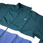 The New Balance Numeric Jacket MJ61W4XCAAV in teal and blue features a white horizontal stripe, durable ripstop fabric, and a front zipper, shown flat on a white background.