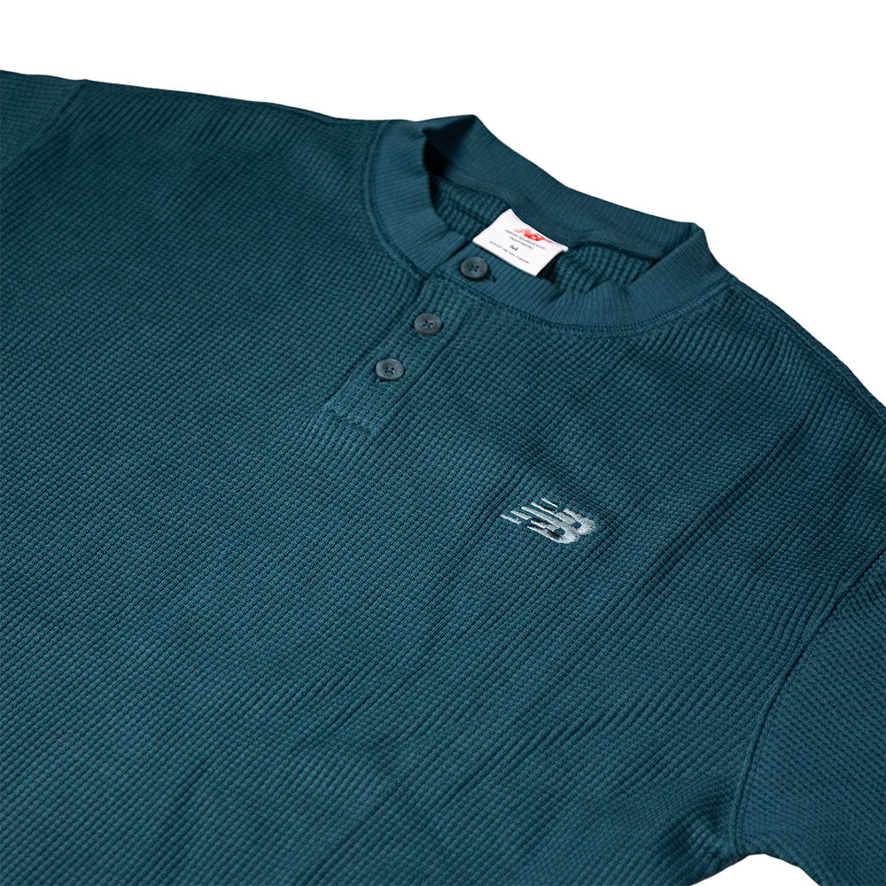 The New Balance Numeric Waffle Knit Tee MT51958AAV is a dark teal short-sleeve henley shirt with a textured waffle knit, three collar buttons, and a small white embroidered logo on the left chest, shown on a white background.