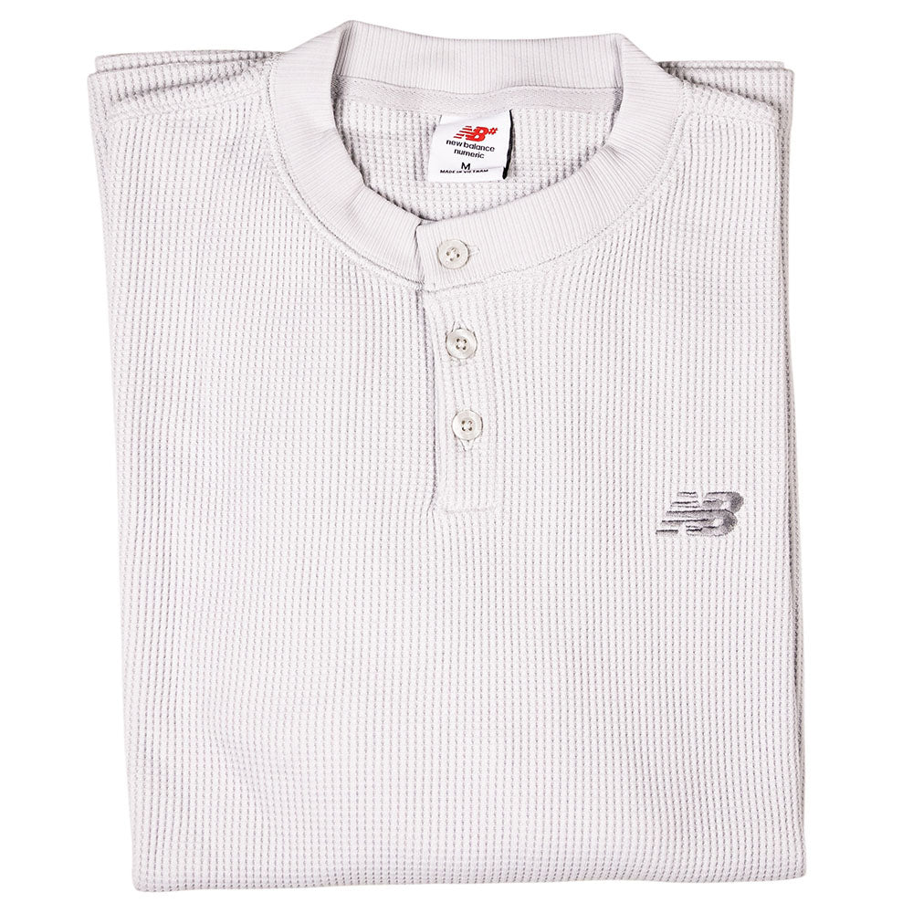 A folded, white New Balance Numeric Waffle Knit Tee MT51958GYM features long sleeves, a waffle-knit texture, three buttons, an embroidered logo on the left chest, and a visible medium size tag.