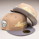 Two beige-and-gray Houston Astros New Era hats: one features a Chalino Skull patch and the other has an Astros logo under the brim. Both Camel Storm 5950 fitted caps boast striking gold and white embroidery.