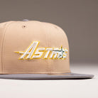 The Chalino Skull Camel Storm Houston Astros New Era 59FIFTY fitted hat features a beige crown, gray brim, and "Astros" embroidered in yellow, white, and gray on the front. The background is plain and out of focus.