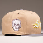 The Chalino Skull Camel Storm Houston Astros New Era 5950 Fitted Hat features beige and gray colors, a white embroidered Chalino Skull patch on the side, and "Astro" in yellow and white script on the front.