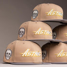 A stack of Chalino Skull Camel Storm Houston Astros New Era Hat 5950 Fitted, featuring embroidered skull designs and "Astros" in gold and white on the front, arranged in a pyramid against a neutral background.