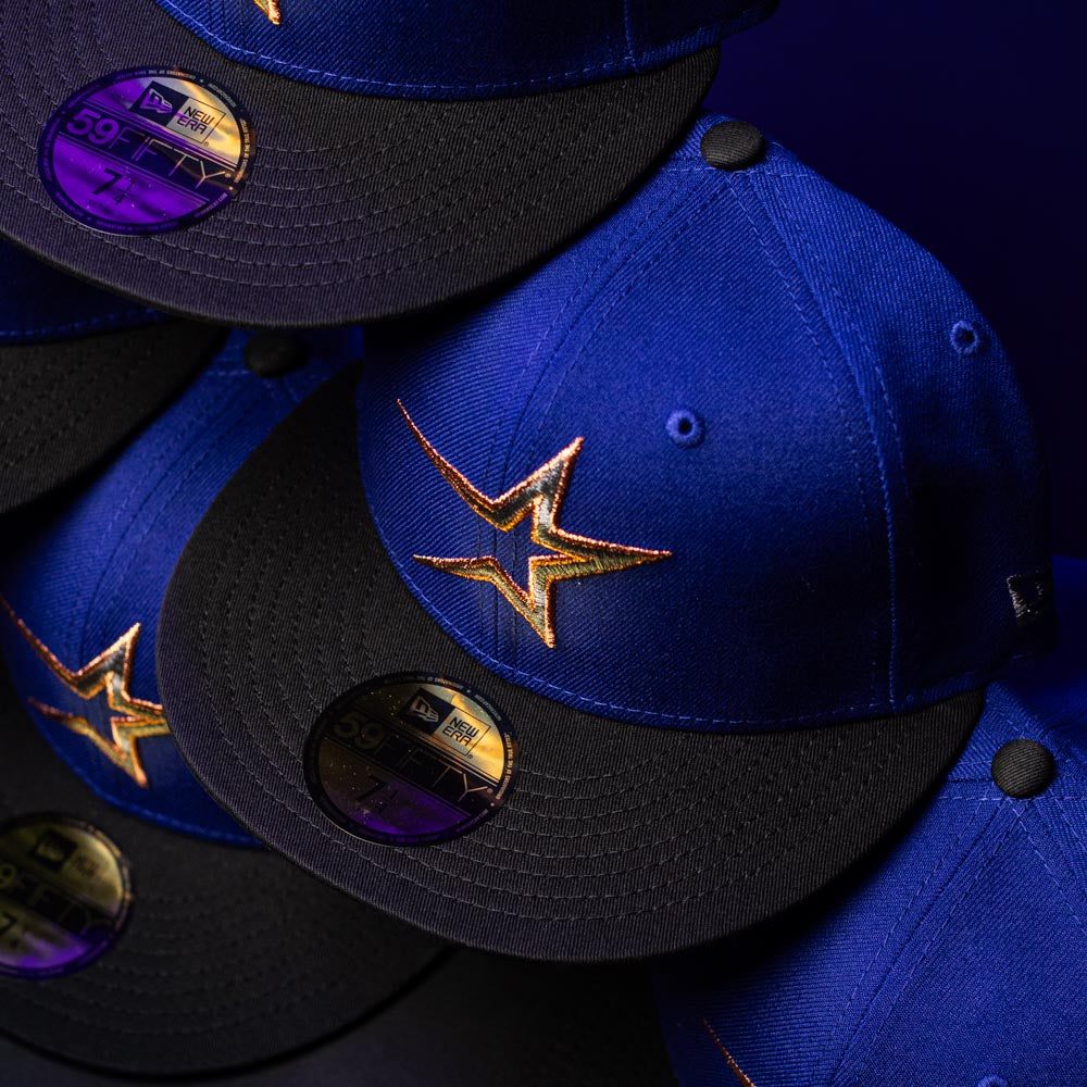 A close-up of stacked H Town North Houston Astros New Era Hat 5950 Fitted caps in blue and black, featuring gold star logos and New Era 59FIFTY authenticity stickers on the brims, set against a dark background.