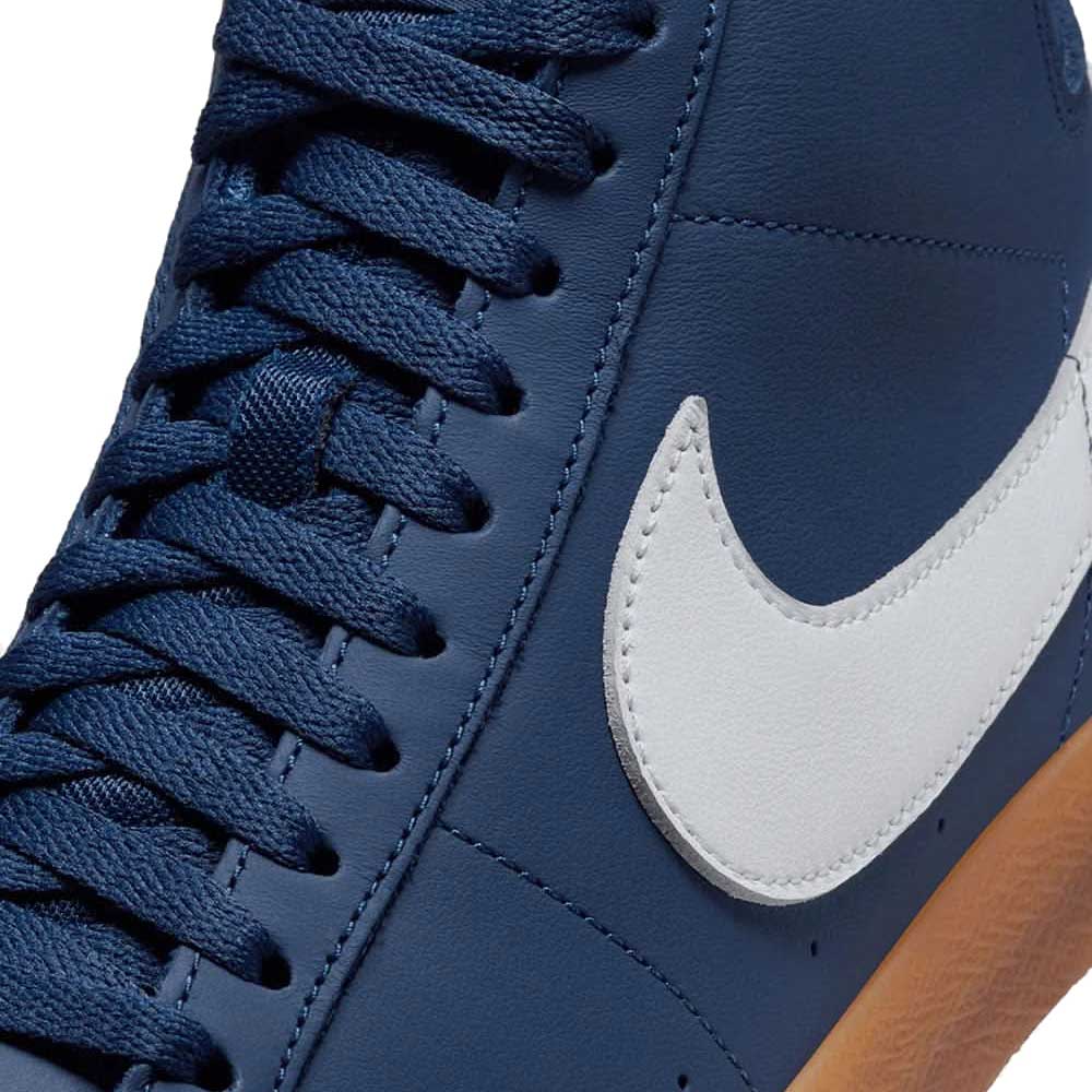 Close-up of the Nike SB Blazer Mid FJ1680400 White Navy Leather Shoes featuring navy blue laces, a white Nike swoosh, gum sole, and responsive Zoom Air cushioning—an excellent pick for skateboarding enthusiasts.