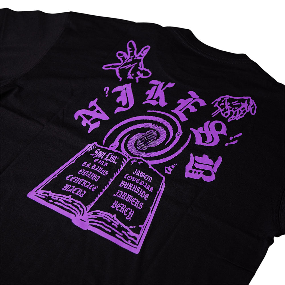 The Nike SB Purple Black Tee IR6747010 is a roomy fit, midweight cotton T-shirt featuring a purple open book graphic with swirling vortex, hand signs, stylized Nike SB text, and city names on the pages for durable daily comfort.