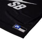Close-up of the Perforated Cropped Black Jersey IF1349010 T-Shirt Nike SB Skateboarding Tee, featuring a white SB logo, blue and white label near the hem, and imported mesh-textured polyester that's machine washable.