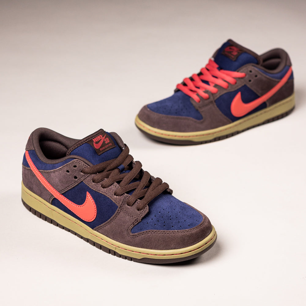 The Baroque Brown Adobe Midnight Navy Dunk Low Pro HQ1625200 Nike SB Suede Shoes feature brown, blue, and purple suede with striking red-orange swooshes and laces, offering a bold look in premium materials on a light surface.